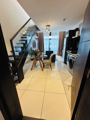 A modern kitchen with a built-in oven and a washing machine, a dining area with a round table and chairs, and a staircase leading to an upper floor. - Phil's Properties At Embassy Gardens GH (Accra)
