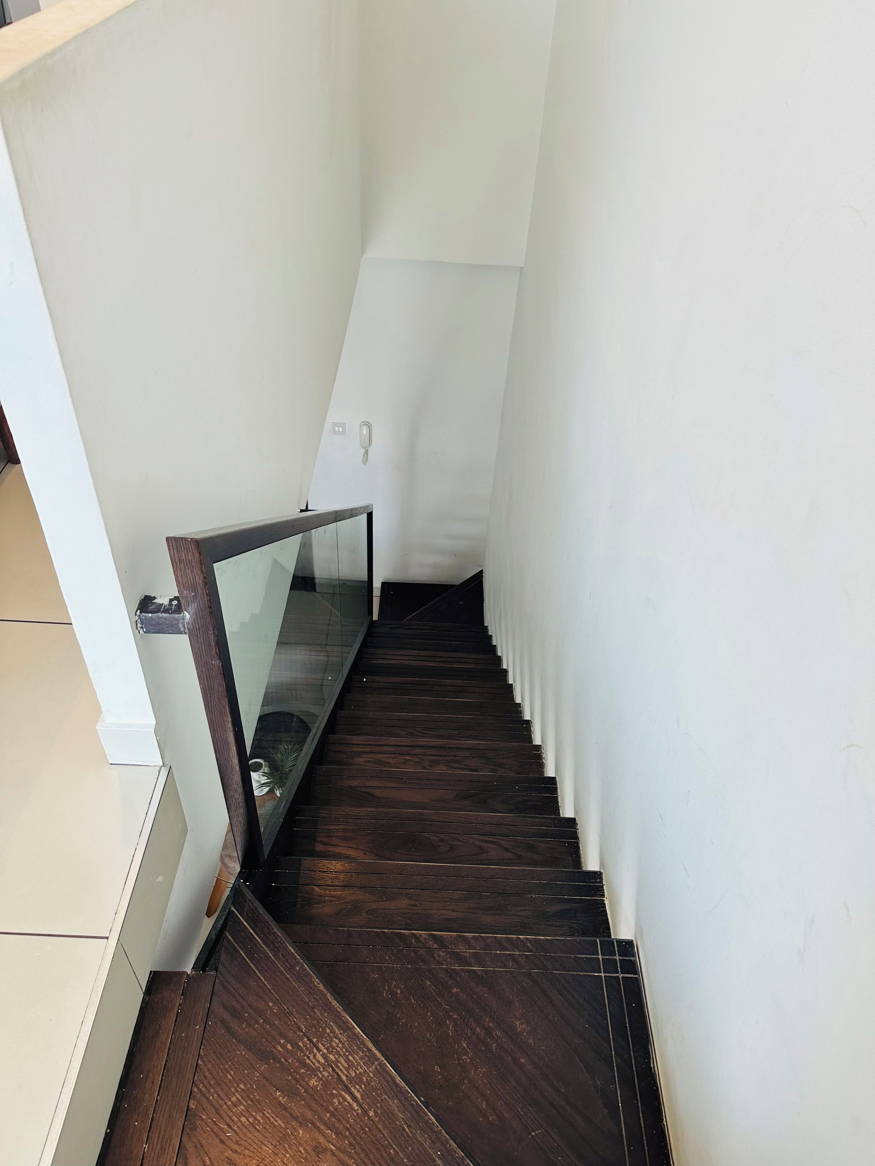 Una escalera con escalones de madera oscura y barandilla de vidrio.