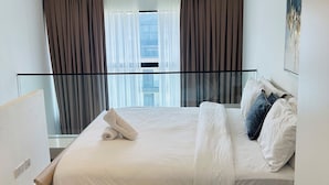 A hotel room with a bed, a bedside table, a nightstand, a window with curtains, and a view of the city. - Phil's Properties At Embassy Gardens GH (Accra)