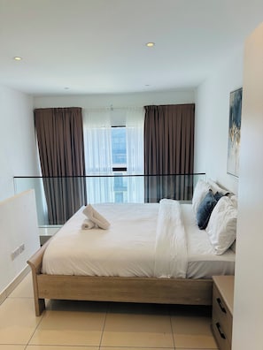 A hotel room with a bed, a bedside table, a nightstand, a window with curtains, and a view of the city. - Phil's Properties At Embassy Gardens GH (Accra)