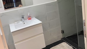 A bathroom with a white sink, mirror, and a glass shower enclosure. - Phil's Properties At Embassy Gardens GH (Accra)