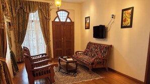 A living room with a sofa, chairs, a coffee table, a rug, a wooden door, and a wall-mounted TV. - Cleety's by MGDC (Kochi)
