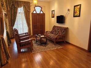 Ein Wohnzimmer mit einer Couch, Sesseln, einem Couchtisch, einem Teppich, einer Holztür und einem an der Wand befestigten Fernseher.