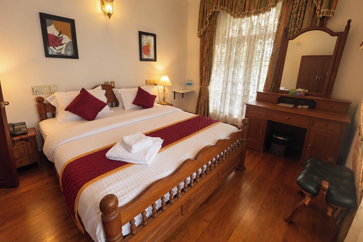 Ein Hotelzimmer mit einem großen Bett, einem Holz-Kopfteil, einem Schreibtisch mit Spiegel und einem Stuhl.