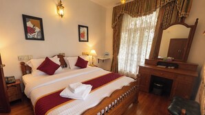 A hotel room with a large bed, wooden headboard, a desk with a mirror, and a chair. - Cleety's by MGDC (Kochi)