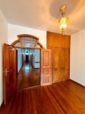 Un couloir doté d’un plancher en bois, d’une porte en bois avec un panneau de verre et d’un luminaire au plafond.