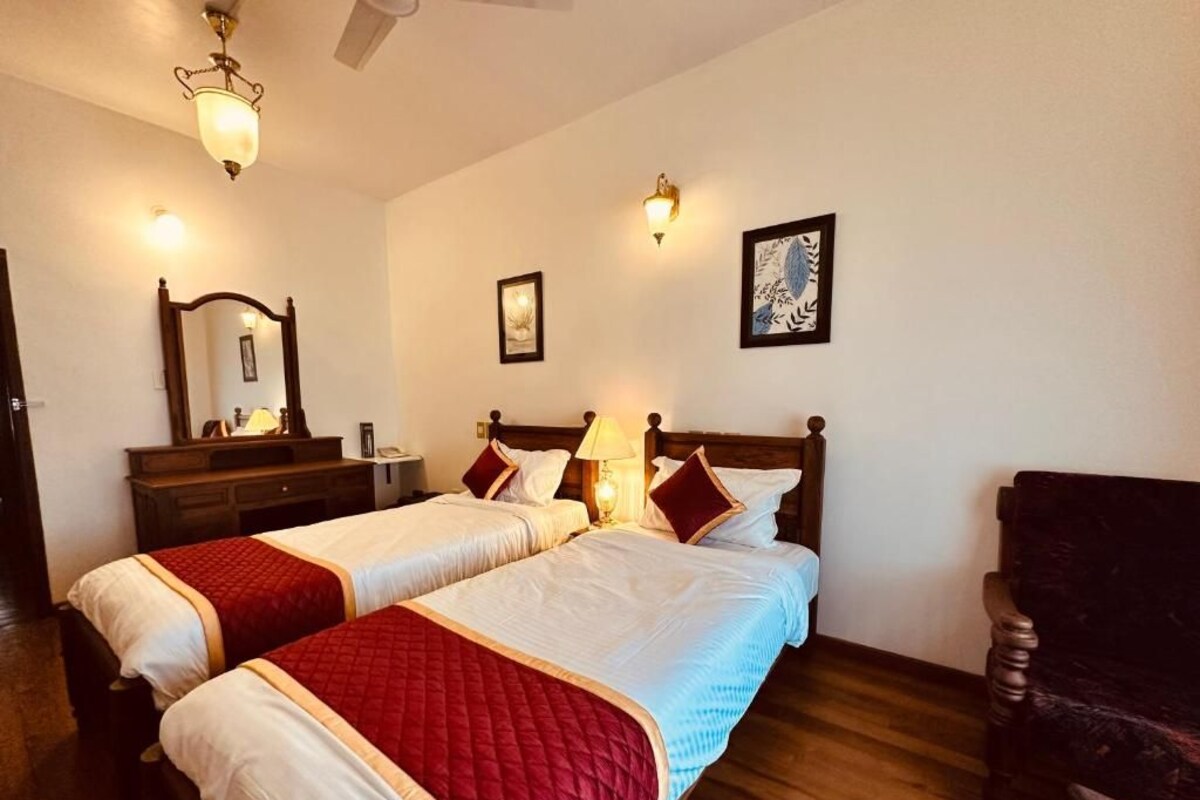 Ein Hotelzimmer mit zwei Betten, Holzboden, einem Sessel, einem Schreibtisch mit Lampe und Wandleuchten.