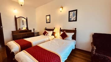 Habitación de hotel con dos camas, suelo de madera, una silla, un escritorio con lámpara y luces en la pared.