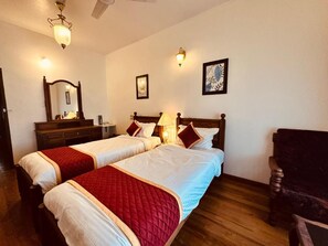 Habitación de hotel con dos camas, suelo de madera, una silla, un escritorio con lámpara y luces en la pared.