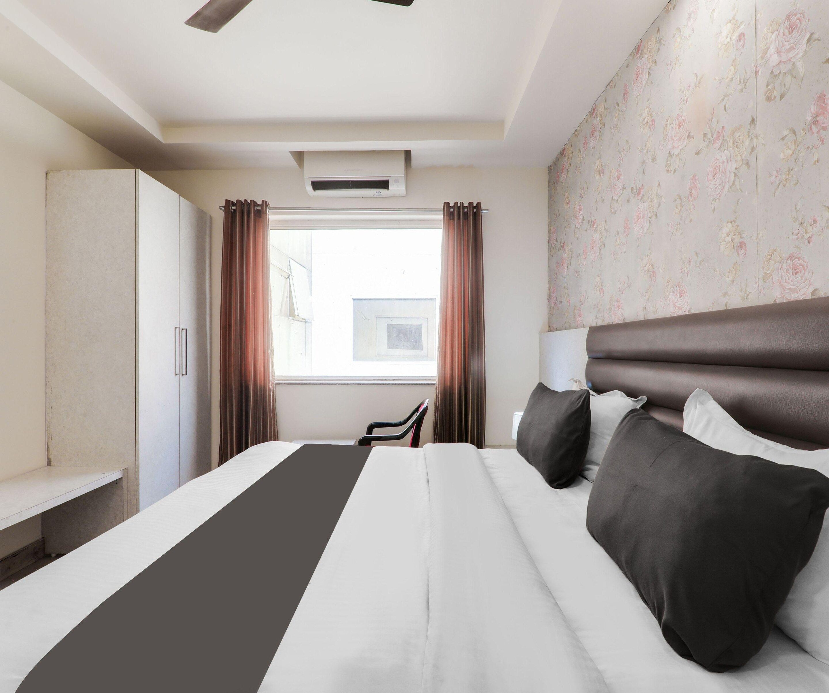 A hotel room with a bed, a desk, a chair, a wardrobe, and a window with curtains.