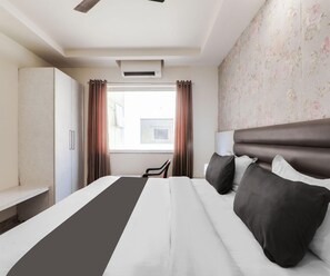 Una habitación de hotel con cama, escritorio, silla, armario y ventana con cortinas.