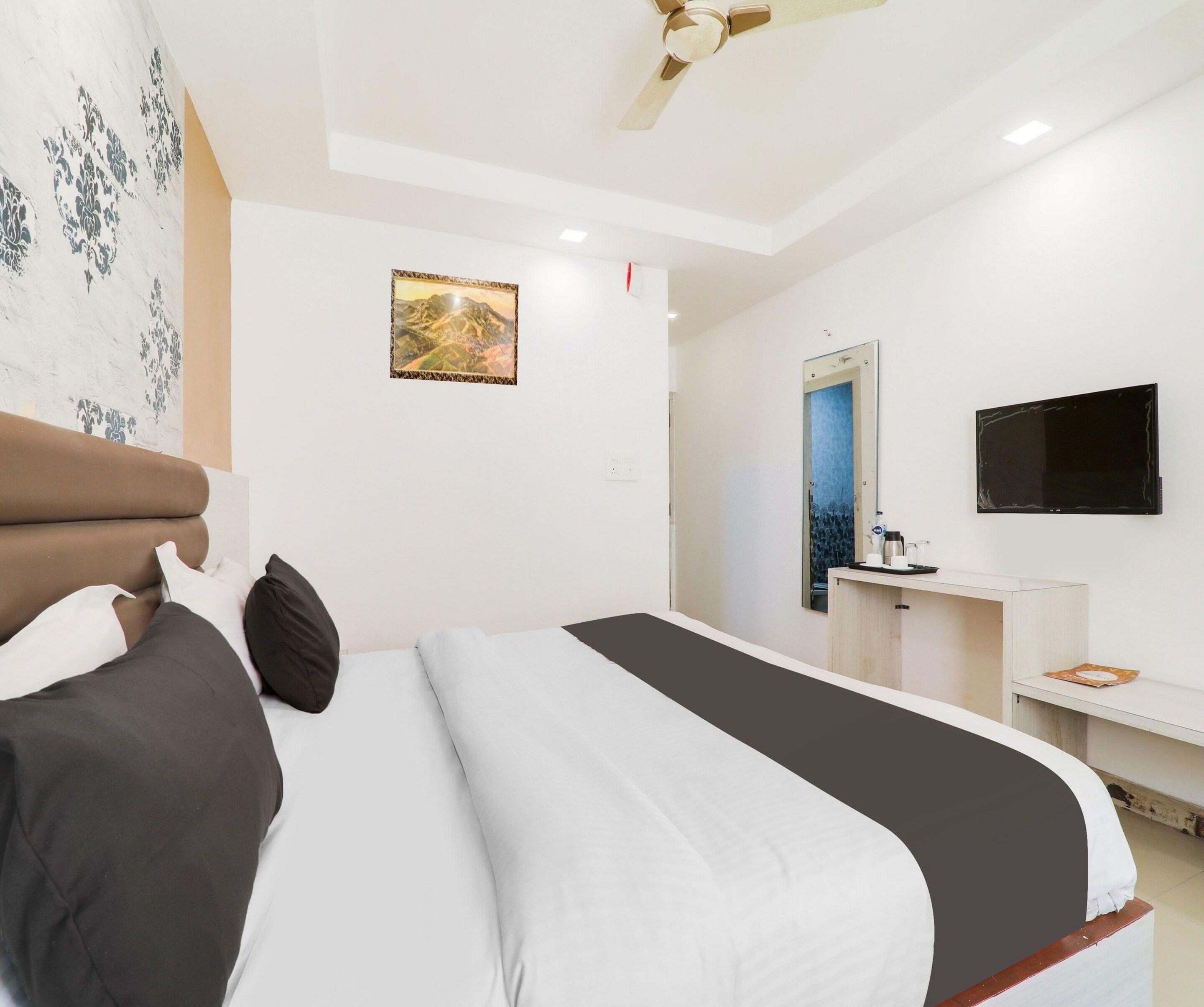 A hotel room with a bed, a desk, a mirror, and a television.