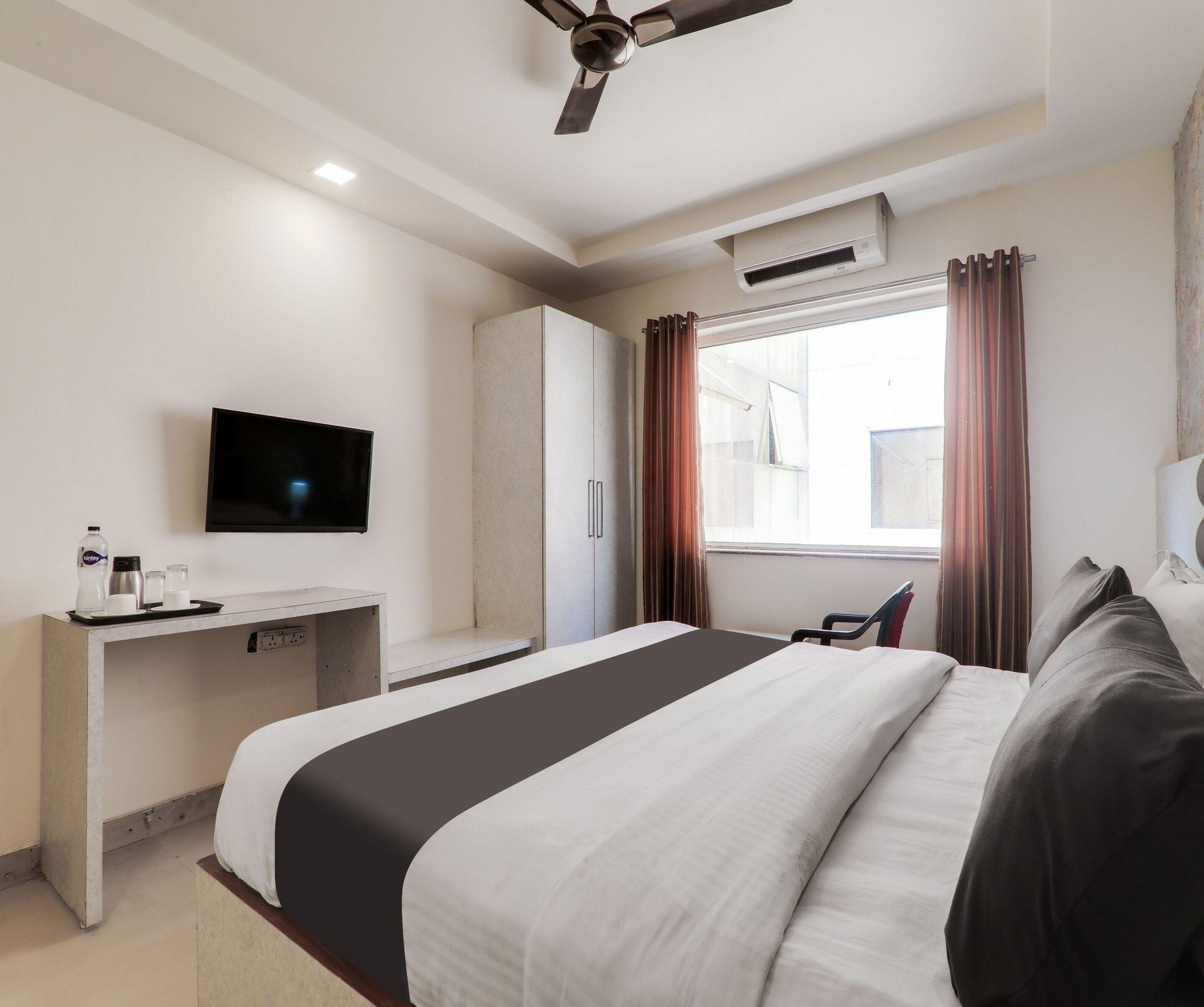 Una camera d'albergo con un letto, una scrivania, una televisione e una finestra con tende.