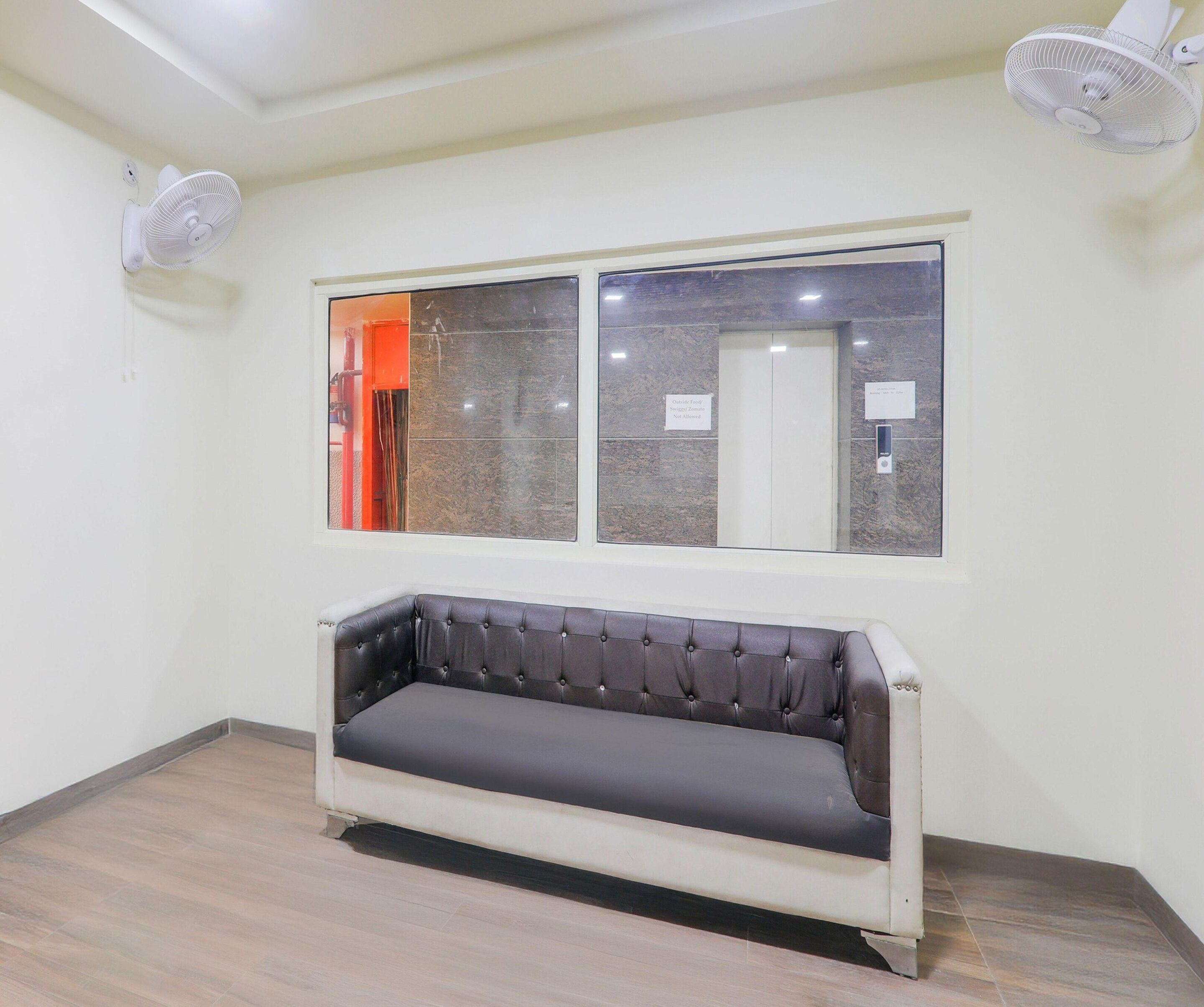 Quarto com sofá, janela e dois ventiladores fixados na parede.