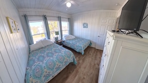 Een kamer met twee bedden, houten vloeren, een witte deur en een kast met een flatscreen televisie.