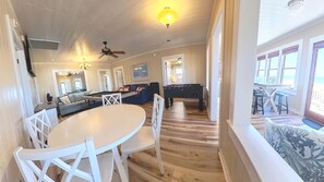 Een ruime kamer met een pooltafel, een eethoek met een ronde tafel en stoelen, een bank en een plafondventilator.