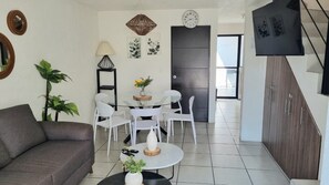 A living room with a sofa, a dining table with chairs, a coffee table with a vase, and a TV mounted on the wall. - Casa Carmin (El Guaje)