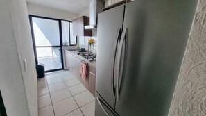 A kitchen with a stainless steel refrigerator, a gas stove, and a sliding glass door leading to an outdoor area. - Casa Carmin (El Guaje)
