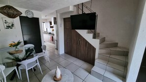 A modern kitchen with a dining area, a staircase, and a flat-screen TV mounted on the wall. - Casa Carmin (El Guaje)