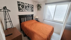 Une chambre à coucher comprenant un lit, un bureau, une chaise, une fenêtre et des œuvres d’art murales.