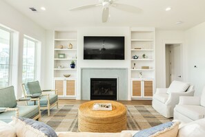 A modern living room with a fireplace, white furniture, and a flat-screen TV mounted above it. - Getaway to 7 Saturdays - Beachside! Beautiful New Construction 2nd Row Home (Galveston)