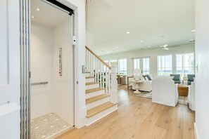 A spacious living area with a staircase leading to an upper floor, large windows, and a view of the outdoors. - Getaway to 7 Saturdays - Beachside! Beautiful New Construction 2nd Row Home (Galveston)