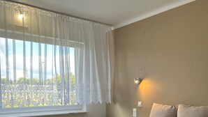 Un dormitori amb un llit, una finestra amb cortines primes, una tauleta de nit i una làmpada penjada a la paret.