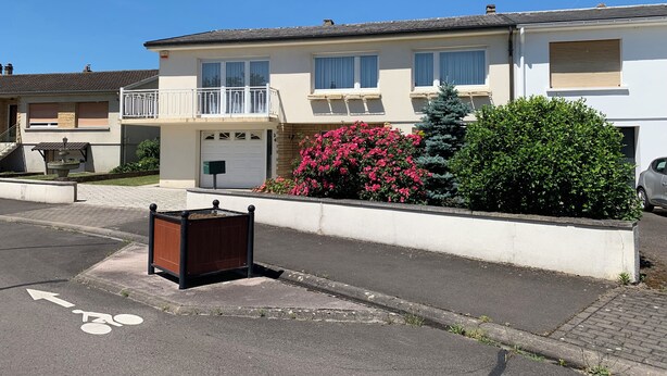 Un edifici residencial amb garatge, un balcó i un jardí amb flors roses.