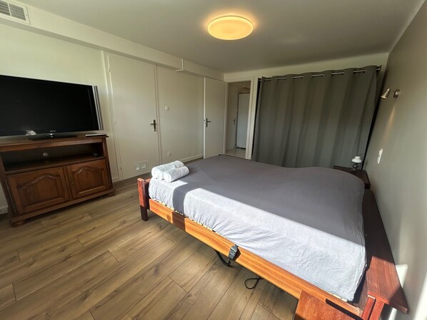 A bedroom with a wooden bed, a television on a stand, and a door leading to another room.