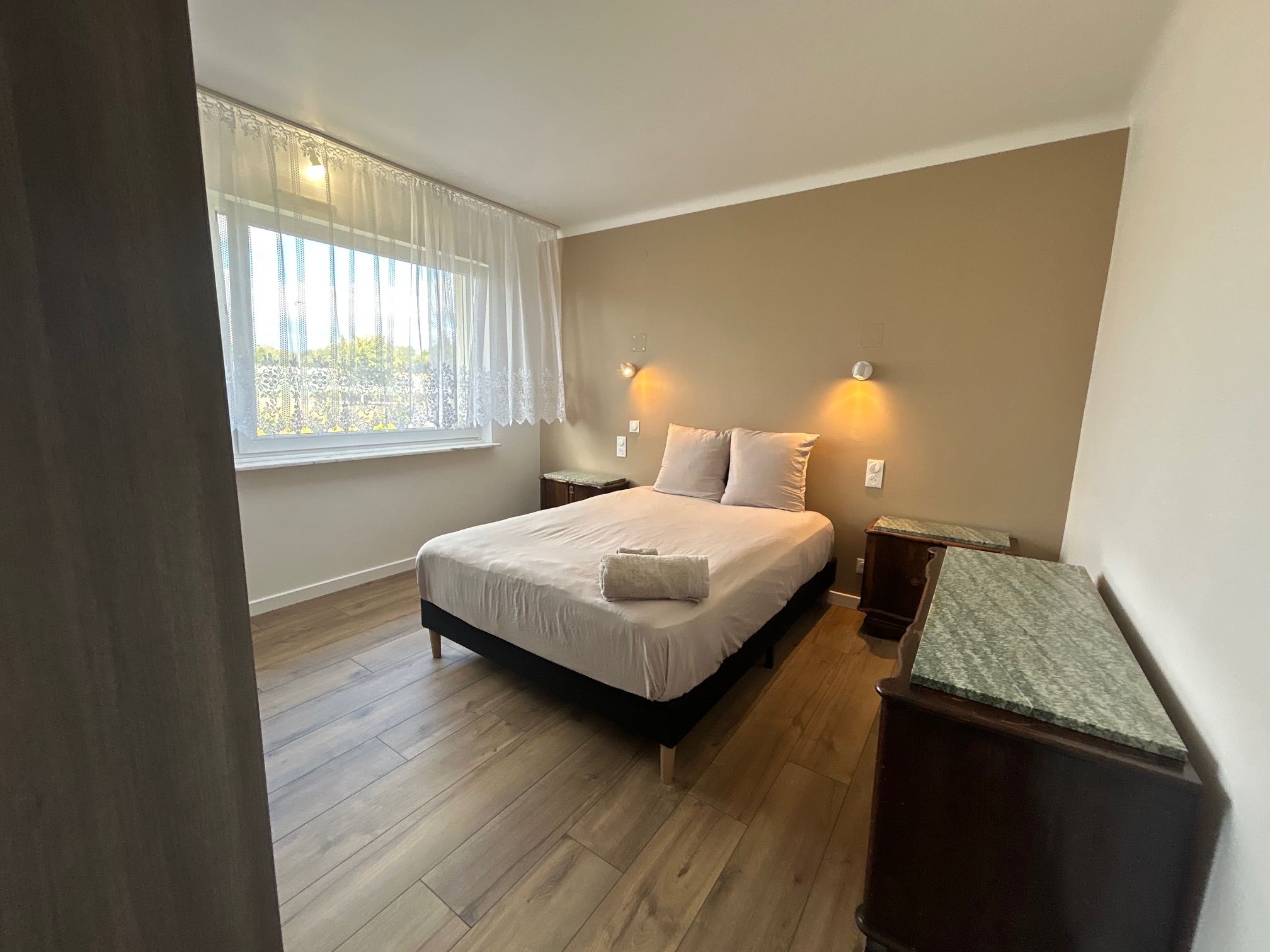 Una camera da letto con un letto, due comodini, una finestra con tende e un tavolo da notte con una lampada.