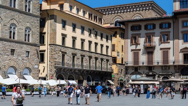 Una piazza vivace con edifici storici, caffè all'aperto e passanti.