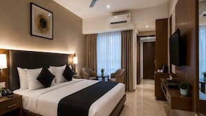 Habitación de hotel con cama, lámparas de noche, ventilador de techo, aire acondicionado, televisor y una mesita con una planta.