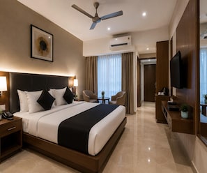 A hotel room with a bed, bedside lamps, a ceiling fan, an air conditioning unit, a television, and a small table with a plant.
