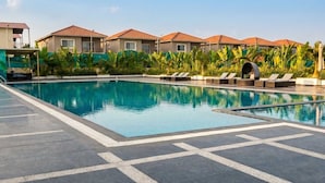 Una piscina con sillas de descanso y un área de estar techada, rodeada de edificios con tejados rojos.