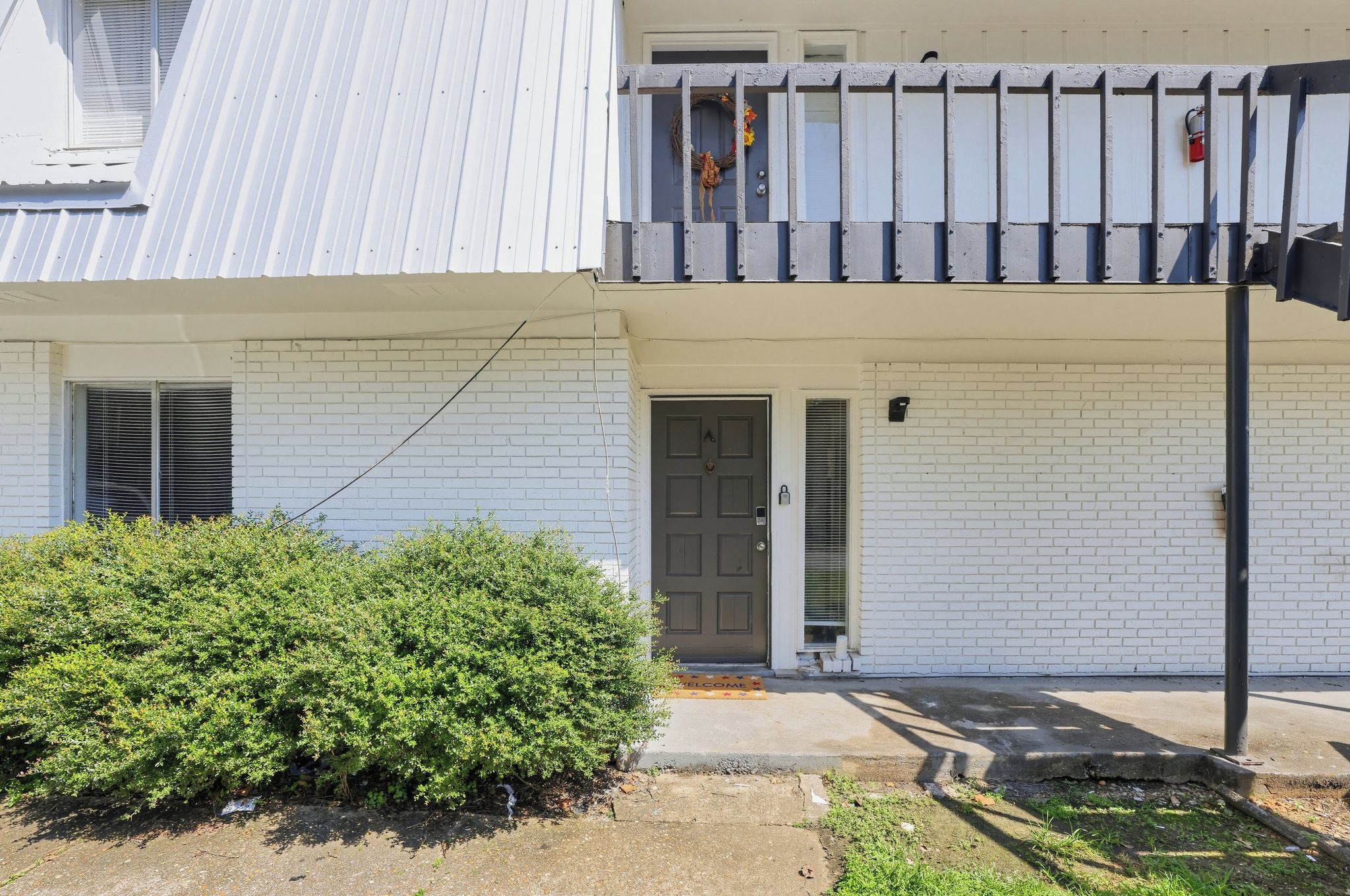 A residential building with a white brick facade, a grey door, and a small balcony with a railing.
