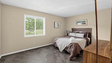 A bedroom with a bed, a window, a framed picture, and a nightstand.