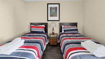 A twin room with two beds, each with striped bedding, a small table with a lamp, and a framed picture on the wall.