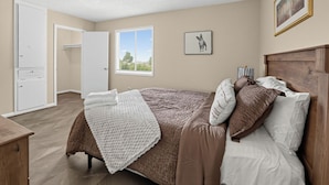 A bedroom with a bed, pillows, a bedside table, a window, and a door. - Spacious Comfort Haven (Montgomery)