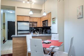 Una cocina moderna con armarios de madera, electrodomésticos de acero inoxidable y un comedor con sillas blancas y una mesa de vidrio.