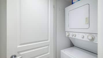 Un lavadero con una lavadora y secadora blancas, una puerta con picaporte plateado y un estante con detergente para la ropa.