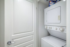 Un lavadero con una lavadora y secadora blancas, una puerta con picaporte plateado y un estante con detergente para la ropa.