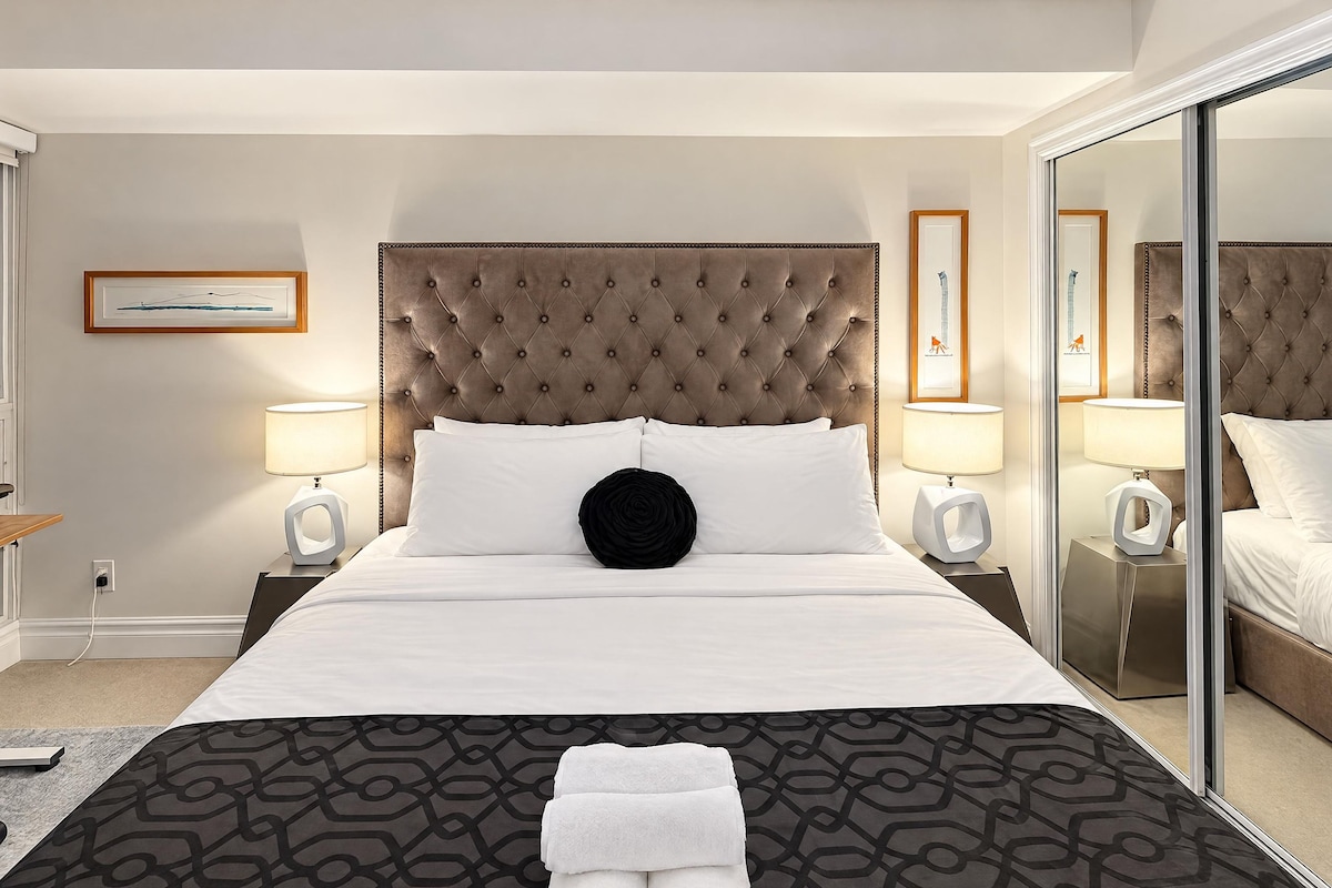 A hotel room with a large bed, two bedside tables with lamps, a mirror, and a patterned bedspread.