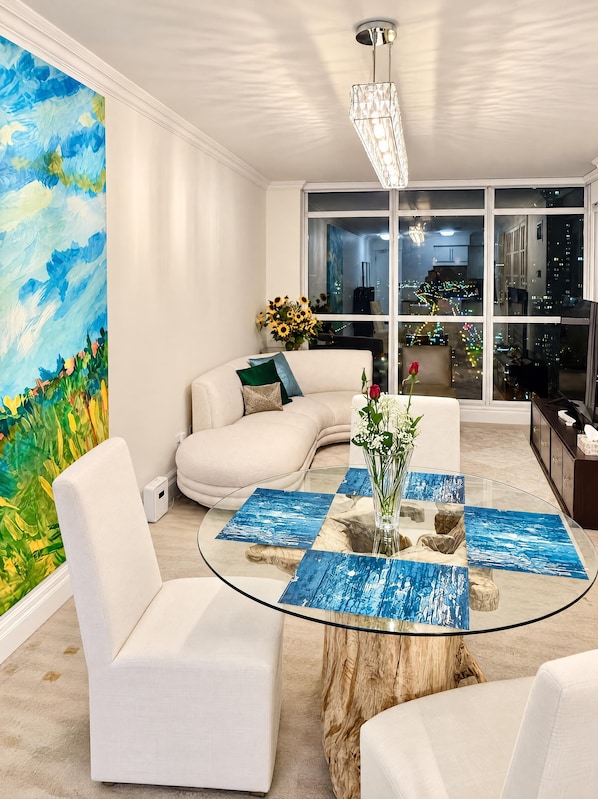 A modern living room with a glass coffee table, white sofas, a large abstract painting, and a city view through large windows. - Downtown Yonge Core Suites (Toronto)