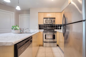 A modern kitchen with stainless steel appliances, wooden cabinets, and a marble countertop. - StayToronto - Downtown Yonge Core Suites (Toronto)