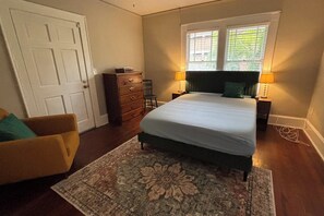 A bedroom with a bed, a dresser, a chair, and a window with blinds. - Historic Riverside Brick Deco | Charming Jax Getaway (Jacksonville)