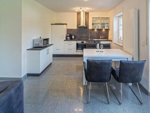 A modern kitchen with white cabinets, a black countertop, and a dining area with two chairs. - Holiday Apartment With 1 Bedroom (Esens)