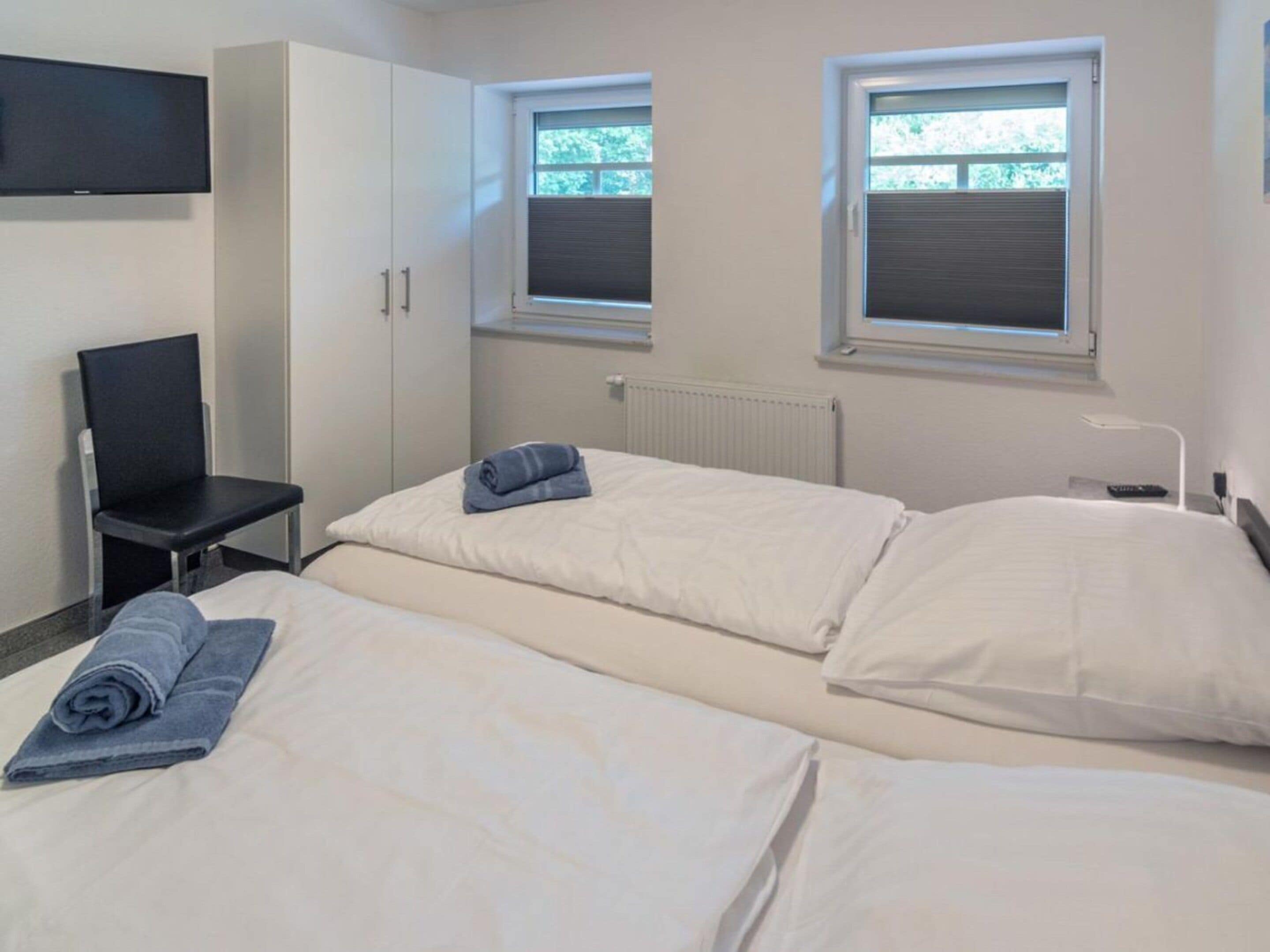 Habitación de hotel con dos camas, una silla, un televisor y ventanas con persianas.