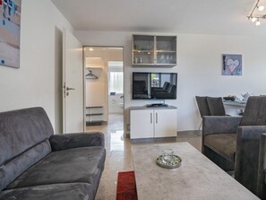 A modern living room with a grey sofa, a coffee table with a candle, and a TV mounted above a cabinet. - Holiday Apartment With 1 Bedroom (Esens)
