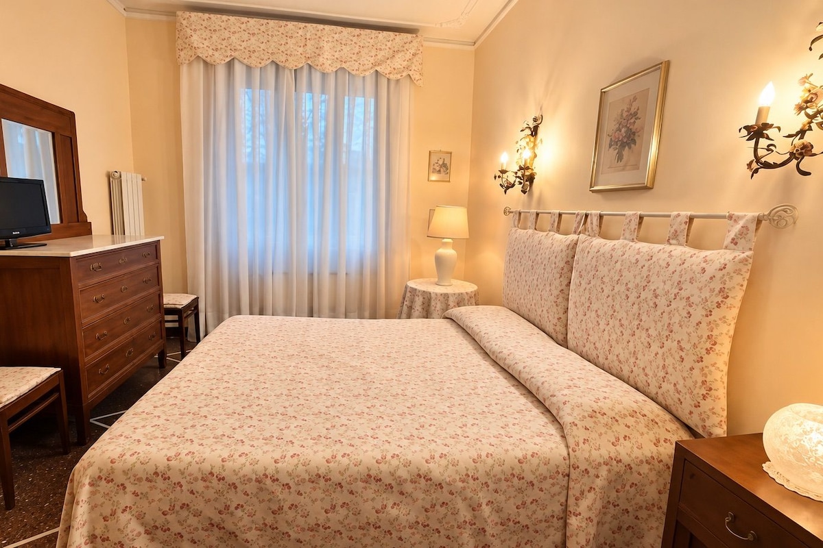 Een hotelkamer met een bed, een bureau, een stoel, een dressoir, een lamp en een wandlamp.