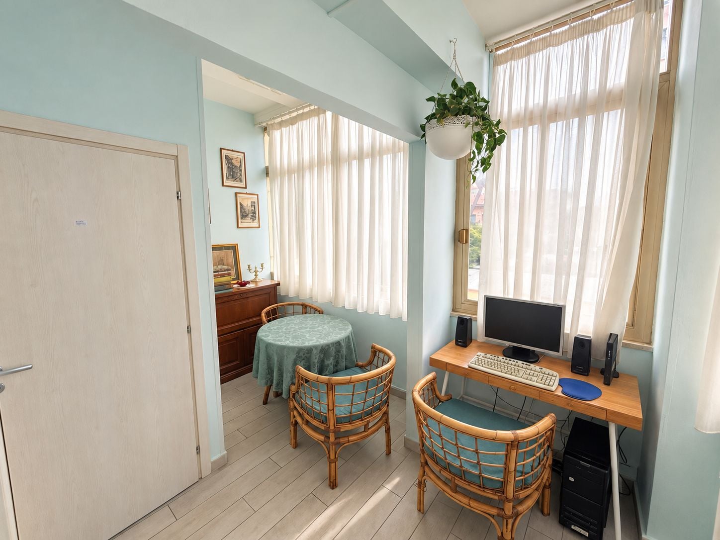 Una habitación con escritorio, computadora, dos sillas, una mesita y una planta colgante.